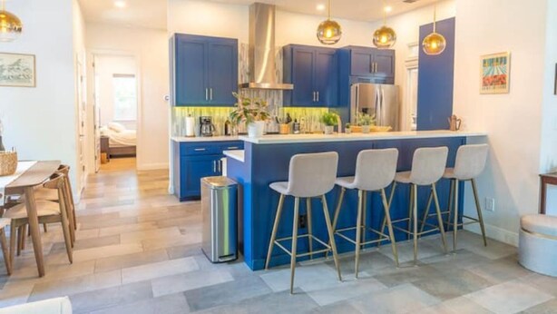 Una cocina moderna con armarios azules, una isla central con taburetes de bar, electrodomésticos de acero inoxidable e iluminación colgante.