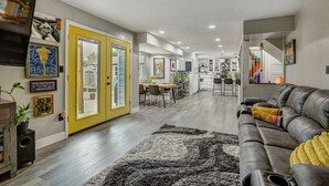 Un salon moderne avec un canapé en cuir, un tapis à motifs et une porte jaune donnant sur un coin repas.