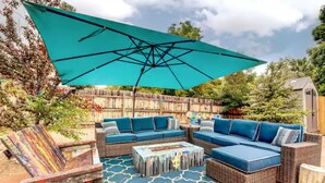 Une terrasse extérieure avec un grand parasol bleu, des meubles en osier et un tapis à motifs.