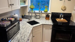 Una cocina con encimeras de granito, armarios blancos, una estufa negra y una ventana con vistas azules.