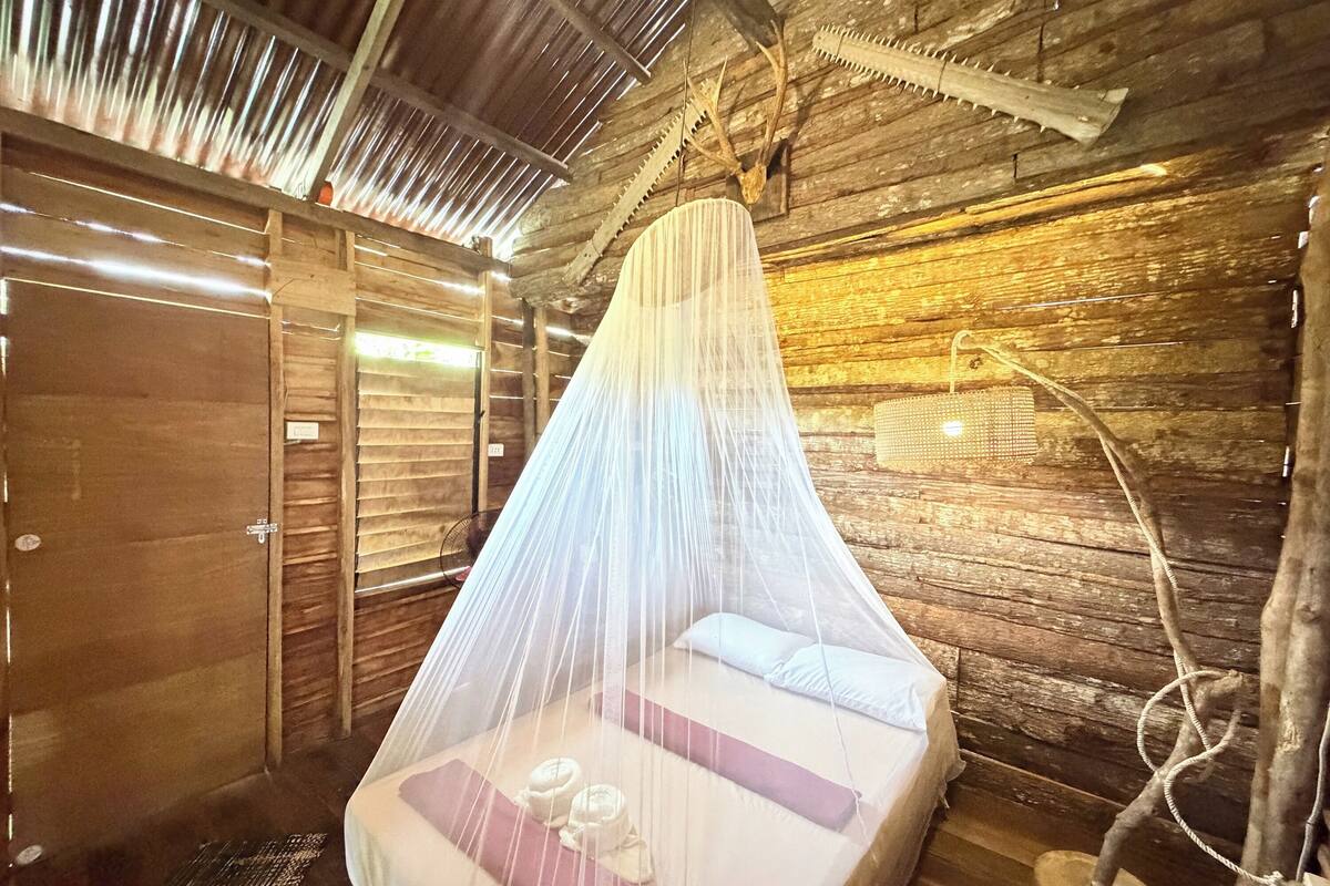 Um quarto rústico de madeira com uma cama sob uma rede de mosquiteiro, teto de madeira e decoração rústica.