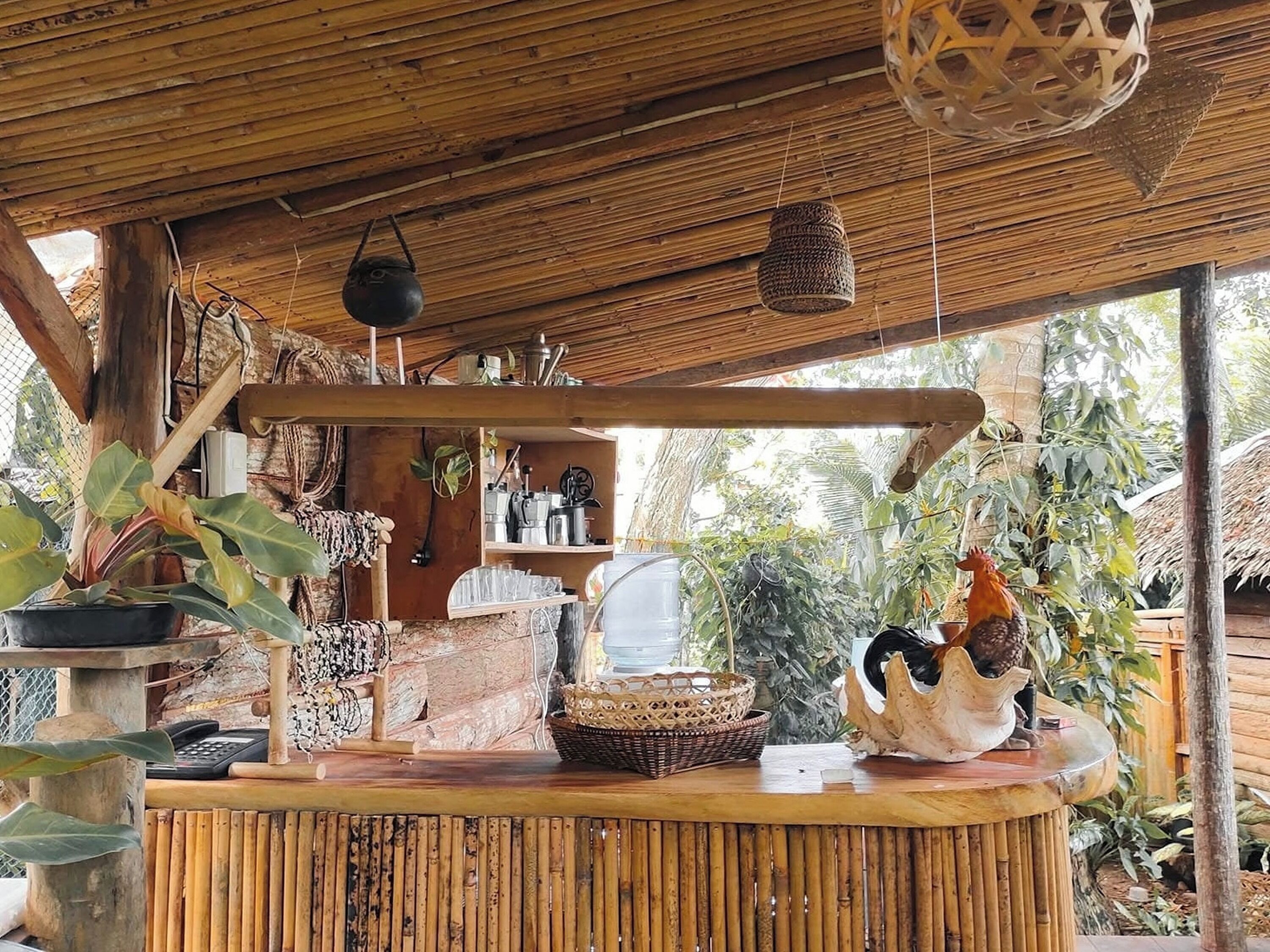 A rustic wooden structure with a thatched roof, a counter with various items, and a rooster statue.