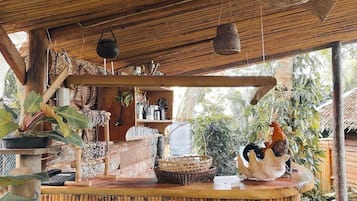 A rustic wooden structure with a thatched roof, a counter with various items, and a rooster statue.