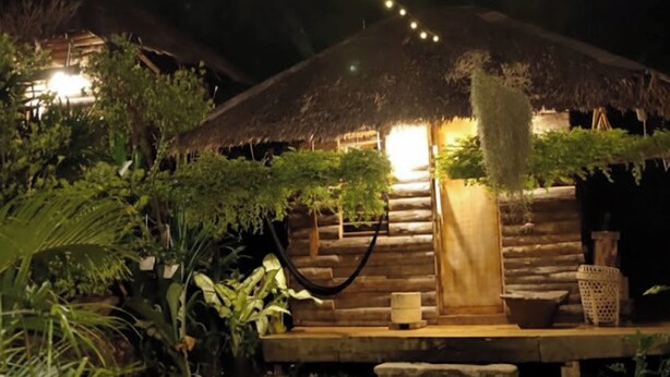 A thatched-roof structure with a wooden staircase leading to a porch, surrounded by greenery. - Payag n' Kapitan, Experience Pinubre Living (Siquijor)