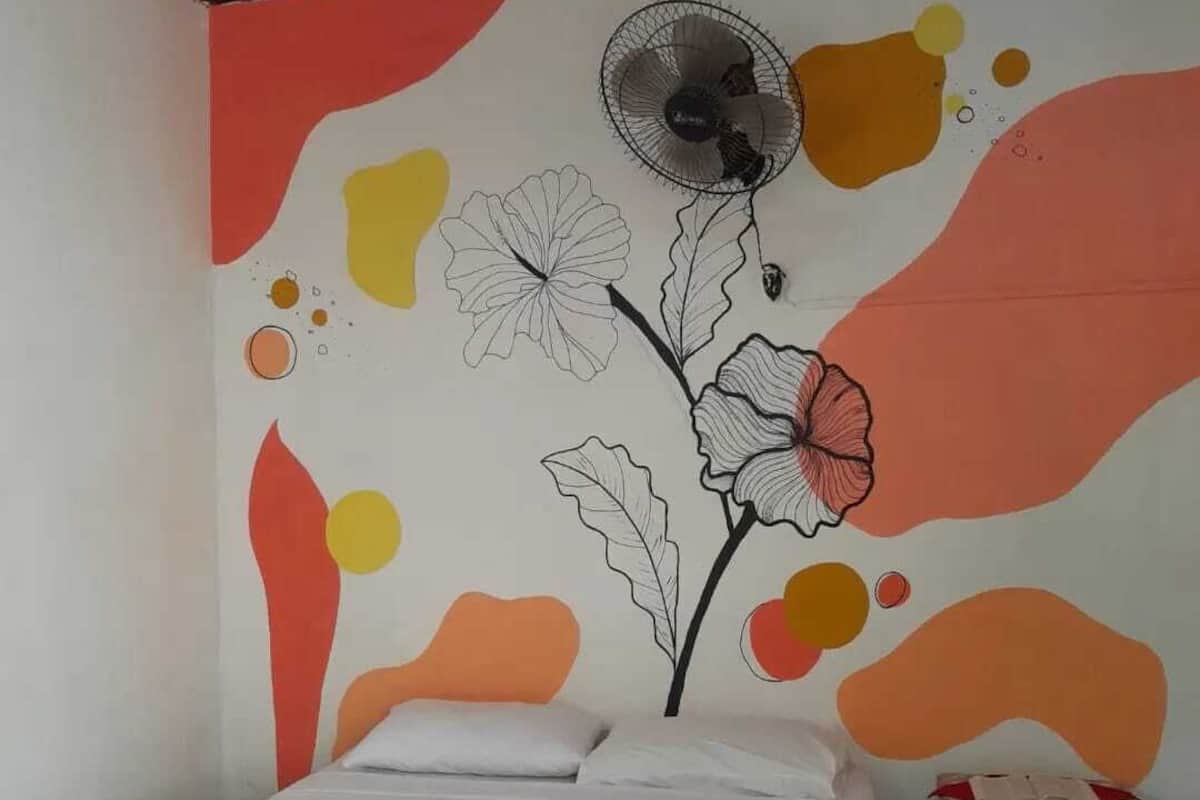 A bedroom with a bed, a small wooden nightstand, and a wall with abstract floral and geometric designs.