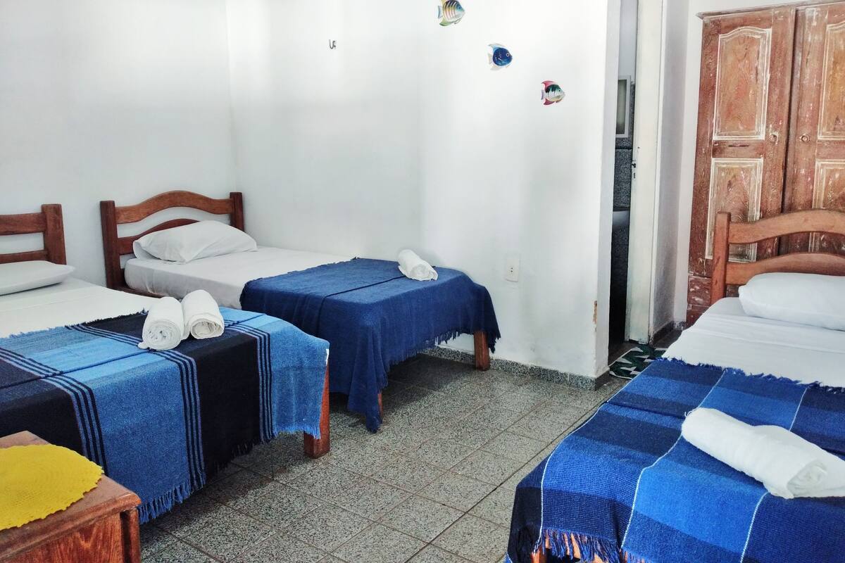 A room with two beds, each with a blue bedspread and white pillows. There are towels on the beds, and a wooden wardrobe is visible in the corner.