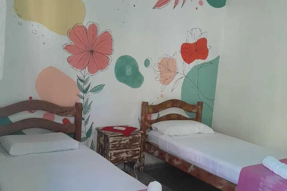 A room with two single beds, a small wooden nightstand, and a wall painted with floral and abstract designs.