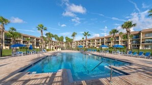 Ein Hotelpoolbereich mit rechteckigem Pool, Liegestühlen und Palmen.
