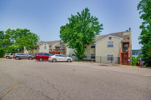 Un quartier résidentiel composé d’une rangée de maisons de ville, d’un parking où sont garées deux voitures et, au premier plan, d’un grand arbre.