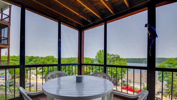 A covered outdoor area with a round table and chairs, overlooking a body of water and a residential area. - Osage Beach Condo w/ Private Deck & Lake Views! (Osage Beach)