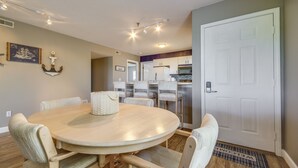 A dining area with a round table and chairs, a kitchen in the background, and a door with a welcome mat. - Osage Beach Condo w/ Private Deck & Lake Views! (Osage Beach)
