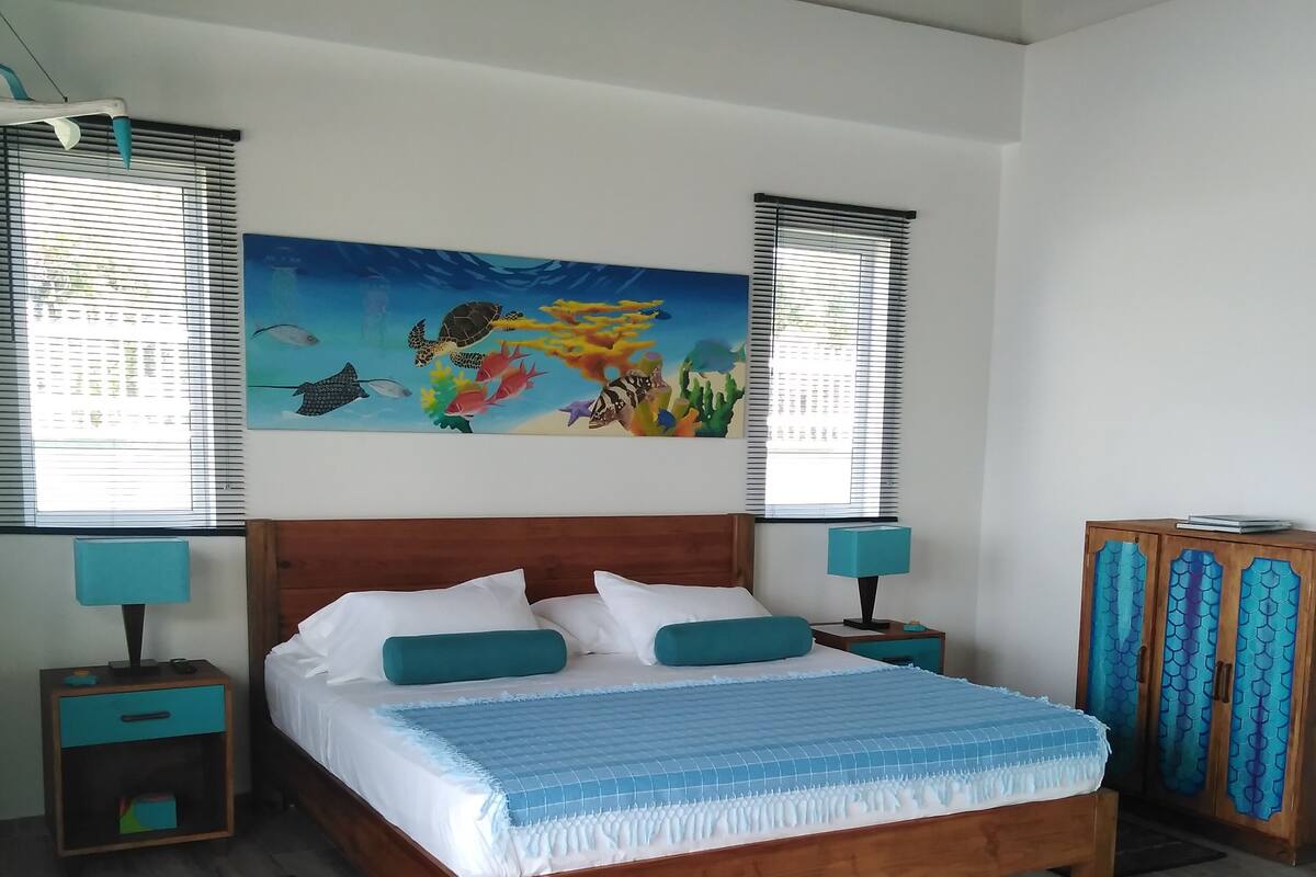 Ein Schlafzimmer mit einem hölzernen Bett, einer Wandmalerei mit Meereslebewesen und einem Schrank mit blauen Vorhängen.