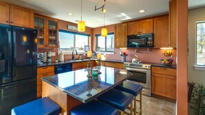 A modern kitchen with wooden cabinets, a large island with bar stools, stainless steel appliances, and a view of the city.