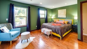 A bedroom with a bed, a blue armchair, a small ottoman, and a window with curtains.