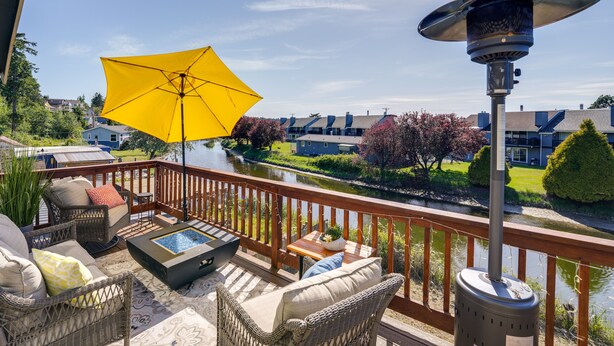 A deck with wicker furniture, a yellow umbrella, and a water feature.