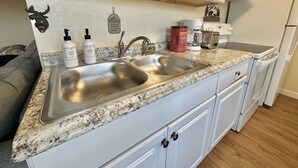 A kitchen with a double sink, white cabinets, a granite countertop, and a coffee maker. - Hot Tub Cozy Cottage in Colorado Springs (Colorado Springs)