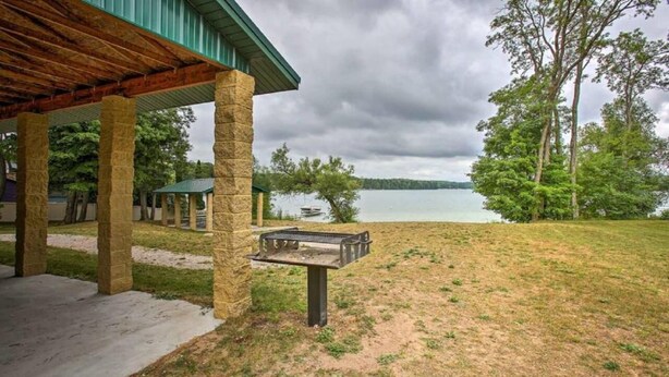 A covered outdoor area with a stone structure, a grill, and a view of a lake. - Grandma's House LA 1-bedroom apartment just 22 minutes to Lake Michigan (Lake Ann)