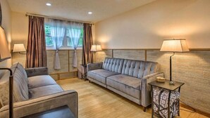 A cozy room with a sofa, a chair, a small table, and a lamp. - Grandma's House LA 1-bedroom apartment just 22 minutes to Lake Michigan (Lake Ann)