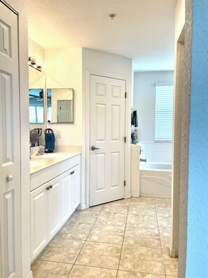 A bathroom with a white door, a sink, a mirror, and a bathtub.