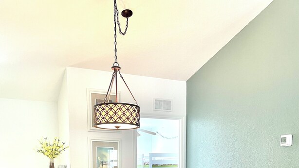 A dining area with a wooden table and white chairs, a hanging light fixture, and a view of the outdoors through a door. - Bright, Safe, Comfortable 3Bdrm in Bradenton, FL.  Pool, Tennis, Golf,  Beaches. (Bradenton)