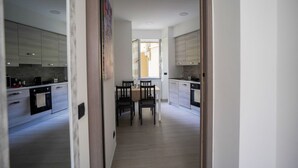 Una cuina moderna amb armaris blancs, una taula de menjador amb cadires i vista a la zona de sala adjacenta.