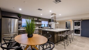 A modern kitchen with a central island, stainless steel appliances, and a dining area with a round table and chairs. - Closest Walk to Old Town, Entertainment District (Scottsdale)