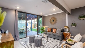 A modern living room with a grey sofa, a coffee table, and a patterned rug. There is a sliding glass door leading to a patio area with outdoor furniture. - Closest Walk to Old Town, Entertainment District (Scottsdale)