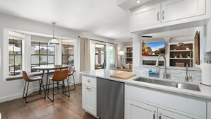 Una cocina moderna con armarios blancos, una isla central y un comedor con sillas.
