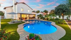 Una casa con piscina, un patio con sillas y un césped bien cuidado.