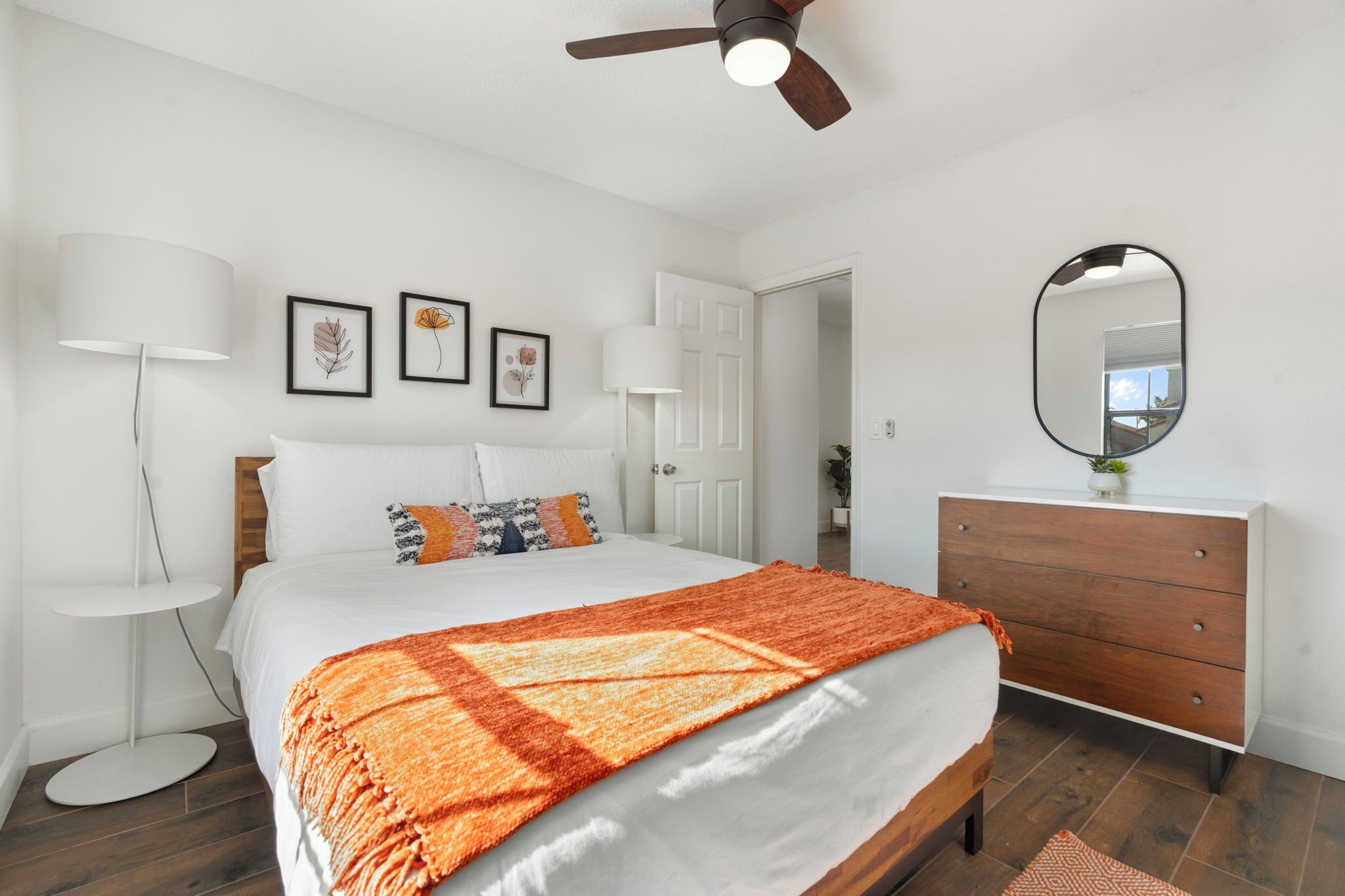 A bedroom with a bed, a dresser, a ceiling fan, and framed artwork on the wall.
