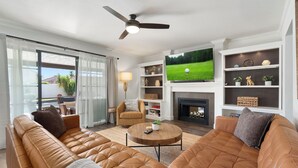 Una sala de estar con sofá, sillón y mesa de centro, televisor montado en la pared y chimenea.