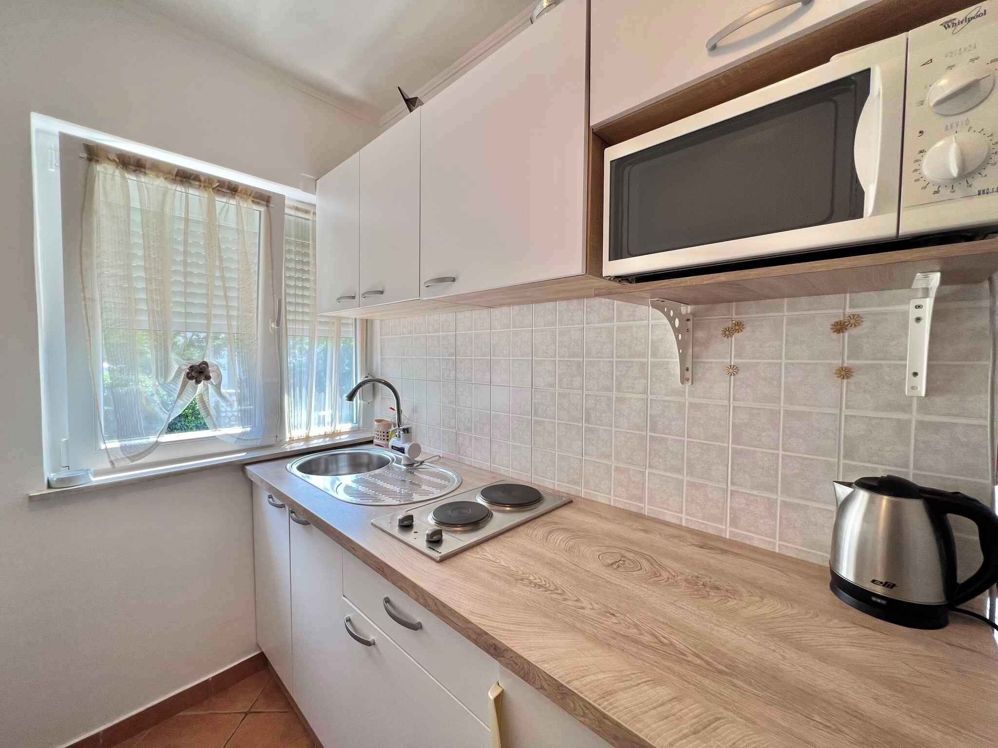 A kitchen with a window, a sink, a stove, a microwave, and a kettle.