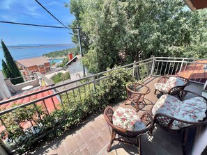 Un balcon avec des fauteuils en osier et une table, d’où l’on peut admirer un plan d’eau et des bâtiments.