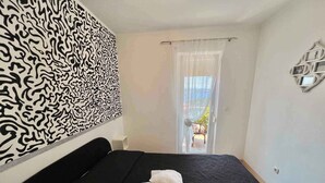 Ein Schlafzimmer mit einem schwarzen Bett, zwei weißen Kissen, einer Wand mit Muster, einem Fenster mit Blick und einem dekorativen Wandbild.