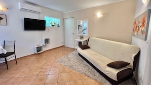 Ein Wohnzimmer mit einer Couch, einem Fernseher, einem kleinen Tisch und einem Sessel.