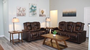 Ein Wohnzimmer mit einer braunen Ledersofa, zwei Holznachttischen und einem Couchtisch. An den Wänden hängen drei Gemälde und auf jedem Nachttisch steht eine Lampe.