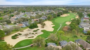 Ein Golfplatz mit Sandbunkern, umgeben von Wohnhäusern und Bäumen.