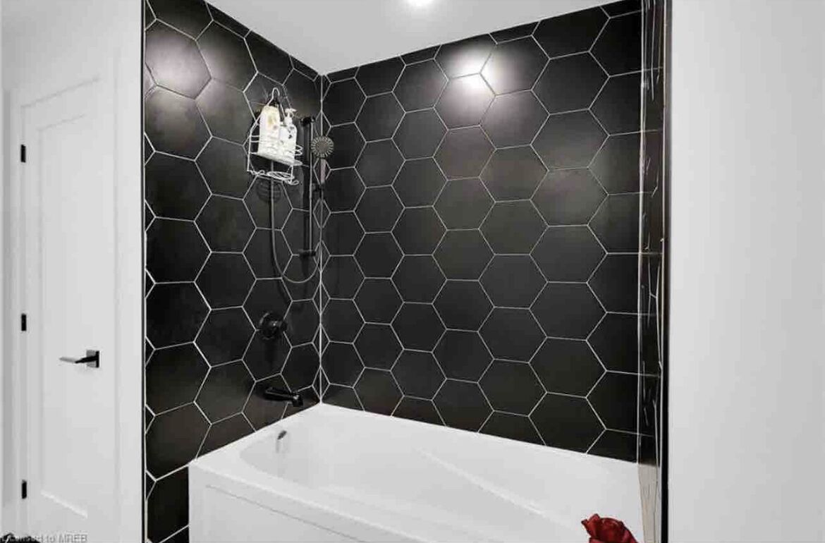 Une salle de bain avec une baignoire blanche, un espace douche et un mur recouvert de carreaux hexagonaux.