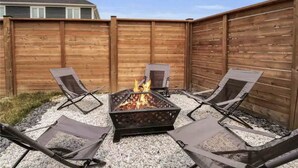 A backyard with a metal fire pit surrounded by four folding chairs.