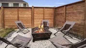 Un jardin avec un foyer en métal entouré de quatre chaises pliantes.