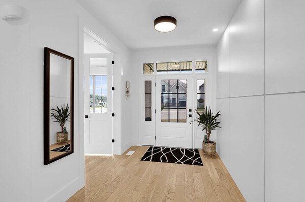 A hallway with a wooden floor, white walls, a large mirror, and two potted plants. - Brand New Modern Luxury Villa (London)