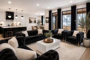 Una sala de estar moderna con una decoración en blanco y negro, que incluye un amplio sofá negro, una mesa de centro blanca y un comedor con una barra negra.