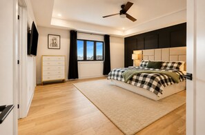 A bedroom with a bed, a ceiling fan, a window with curtains, a dresser, and a framed picture on the wall.