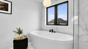 A modern bathroom with a freestanding bathtub, a round pendant light, and a framed picture on the wall. - Brand New Modern Luxury Villa (London)