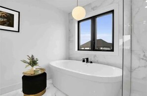 A modern bathroom with a freestanding bathtub, a round pendant light, and a framed picture on the wall. - Brand New Modern Luxury Villa (London)