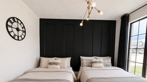 A bedroom with two beds, a wall clock, and a window with a view.