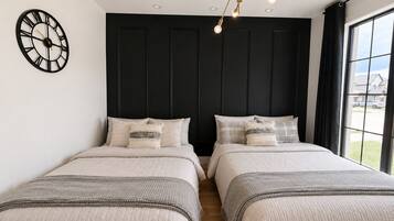 A bedroom with two beds, a wall clock, and a window with a view.