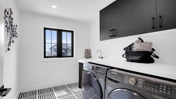 A modern laundry room with a washing machine, dryer, and a black laundry basket on the counter.