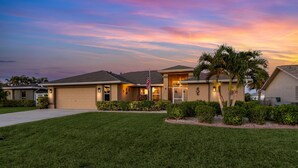 A residential house with a garage, a well-maintained lawn, and a flagpole. - Bikes, Kayaks, Poker, Shuffleboard, Gulf Access, Heated Pool - Comfort on the H2O - Roelens (Cape Coral)