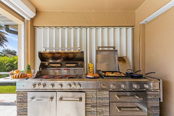 An outdoor kitchen with a grill, oven, and a variety of food items. - Bikes, Kayaks, Poker, Shuffleboard, Gulf Access, Heated Pool - Comfort on the H2O - Roelens (Cape Coral)